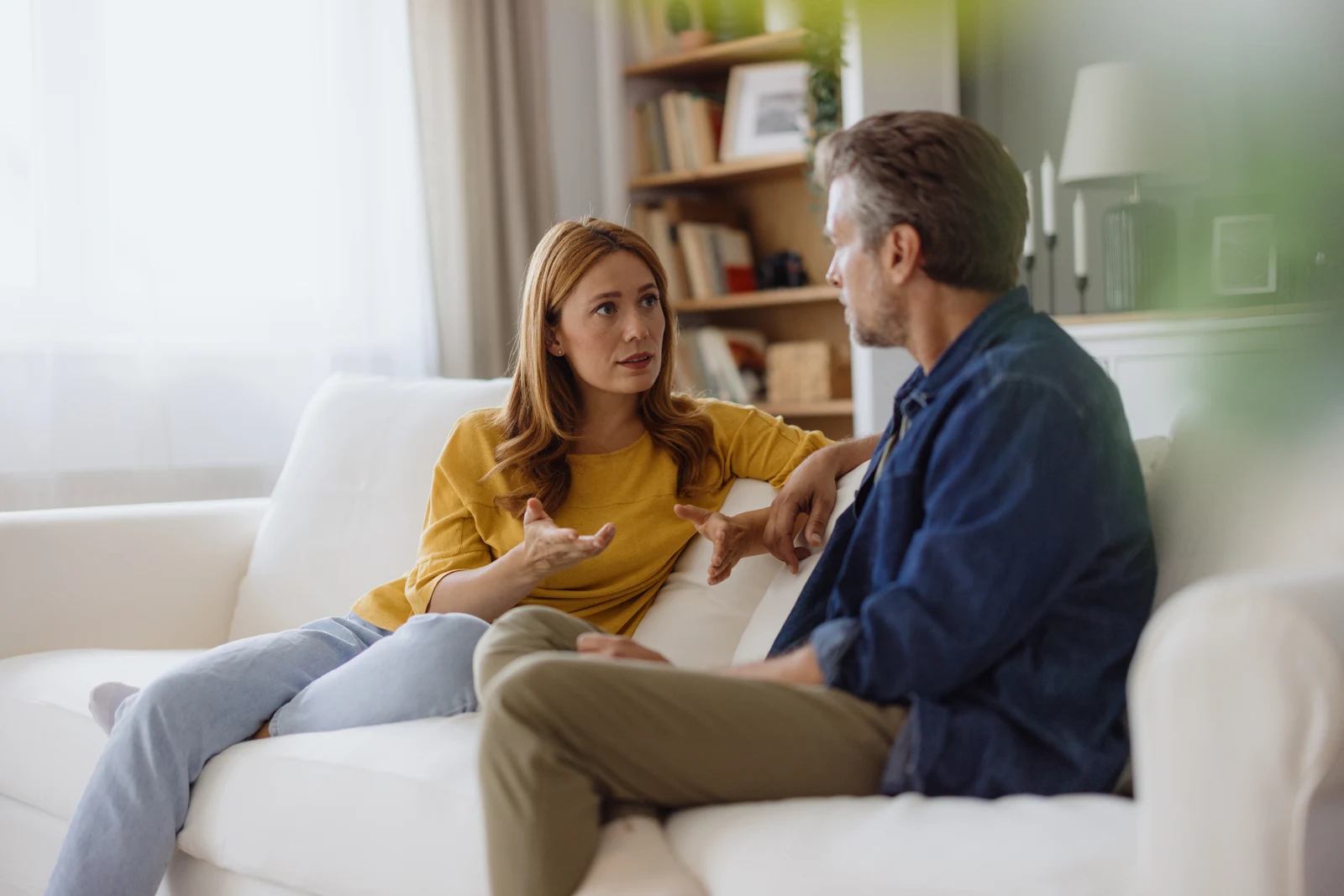 Two adults facing each other in conversation on a sofa.