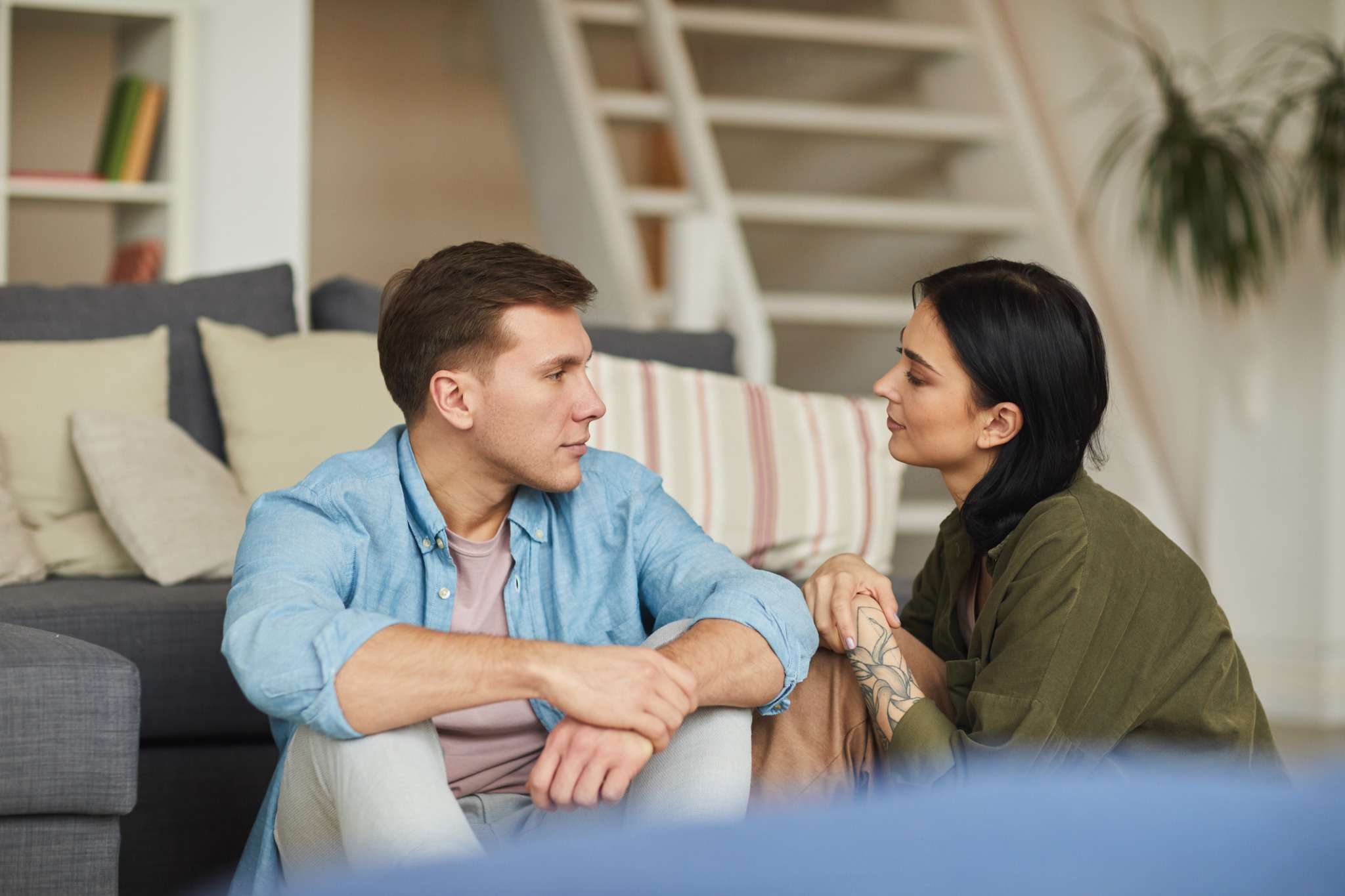 Two adults sitting face to face on the floor beside a sofa.
