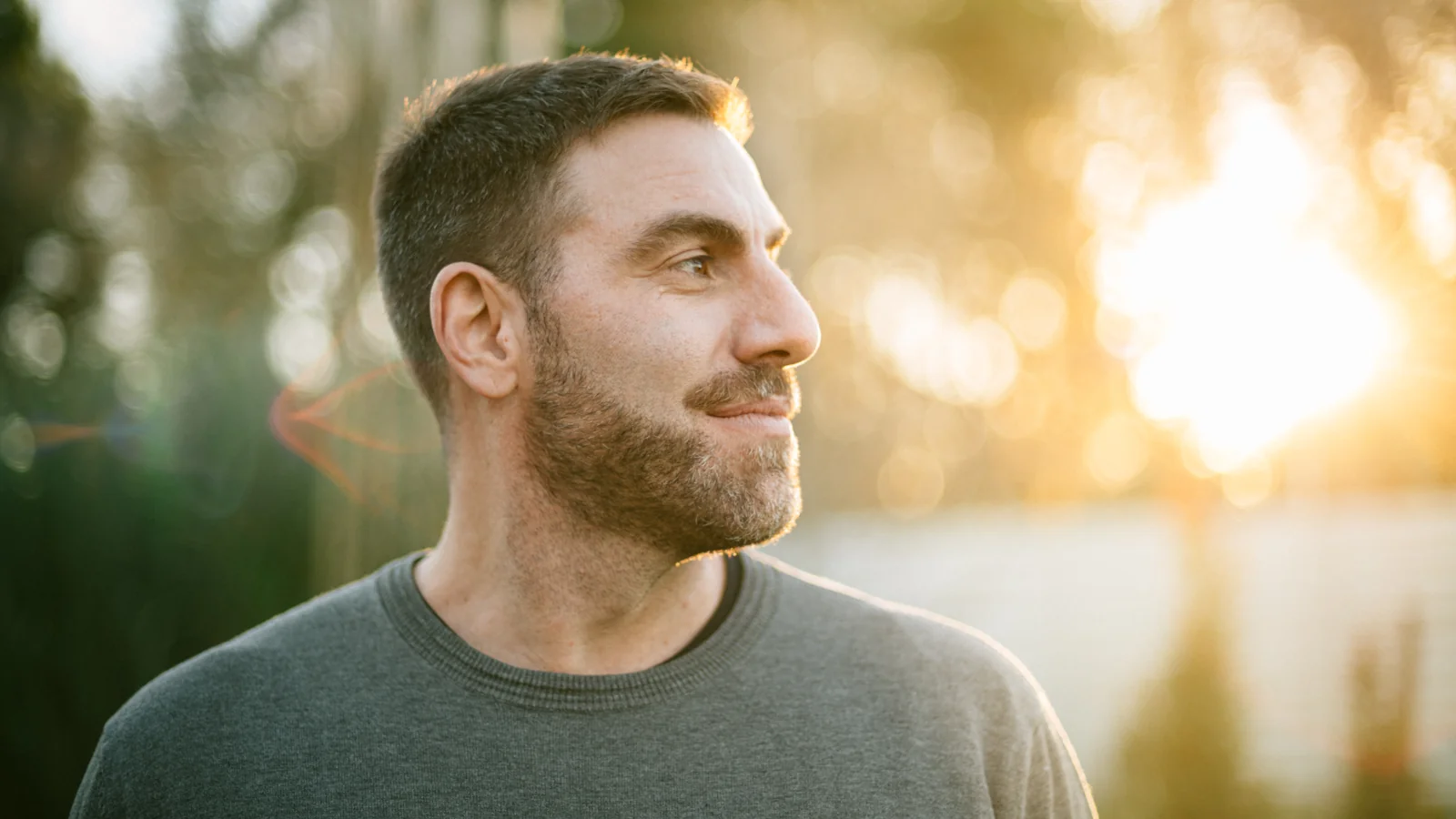 A man outdoors looking toward the light, with trees behind him.