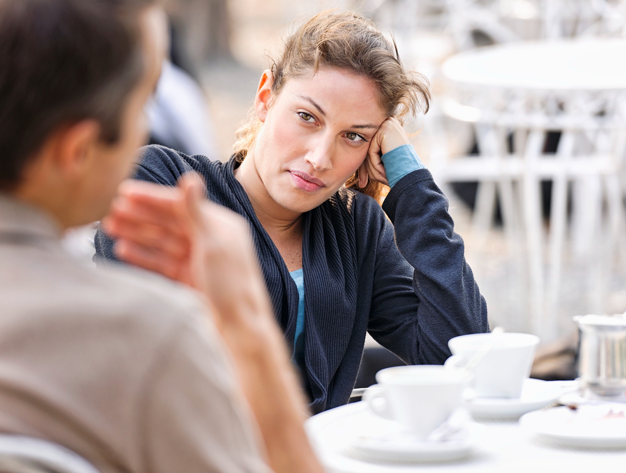 A woman resting her head on her hand while listening to another person at an outdoor café.