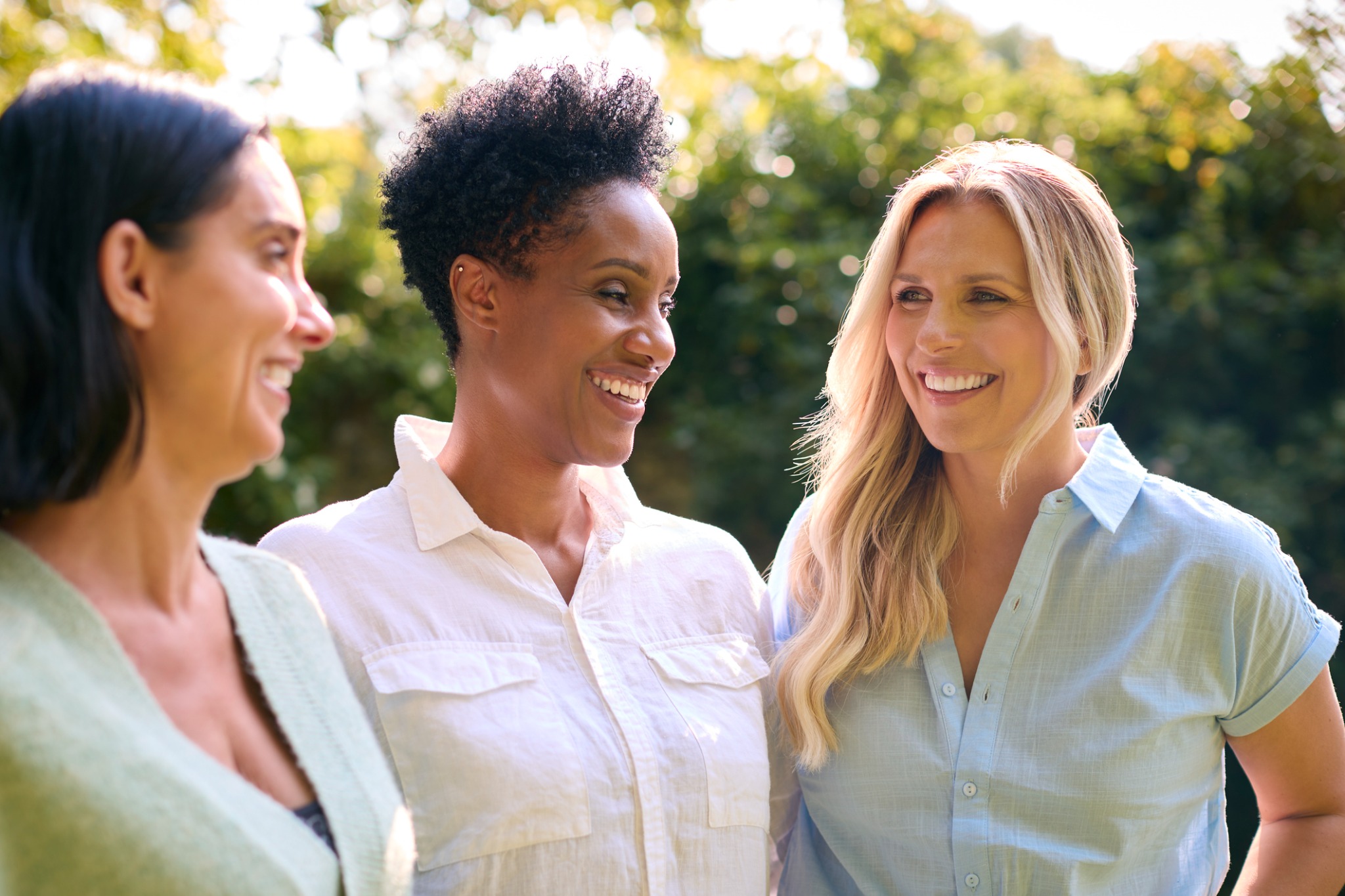 Three women smiling together outdoors in warm light.