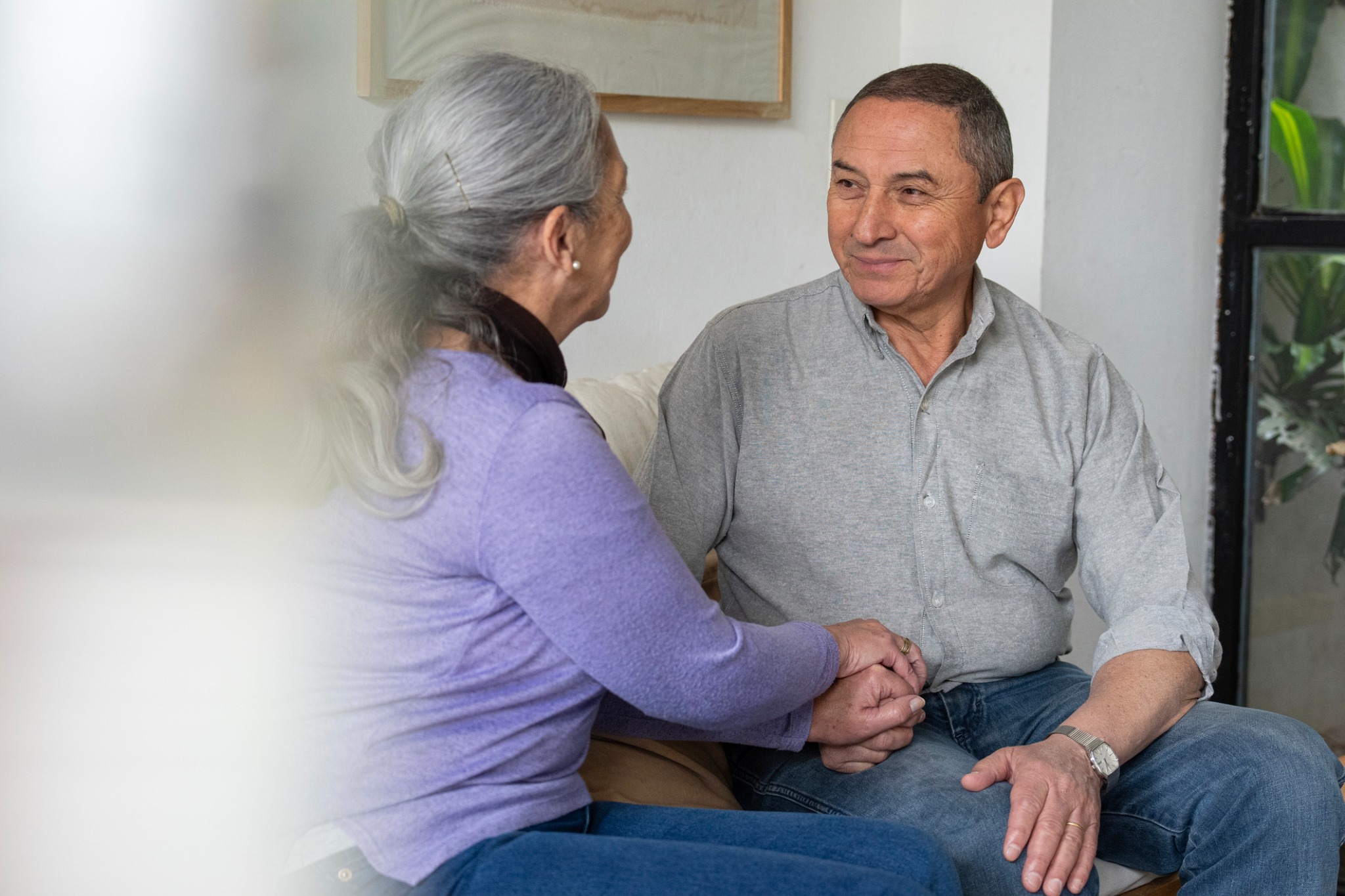 Two older adults holding hands while seated together in conversation.