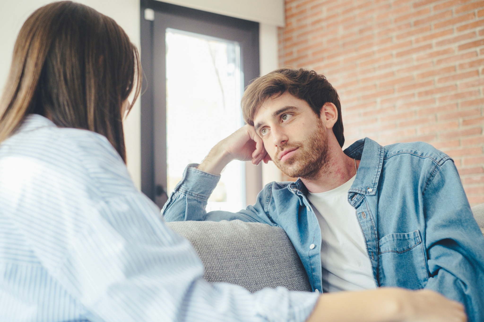 Two adults sitting on a sofa and looking toward one another during a conversation.
