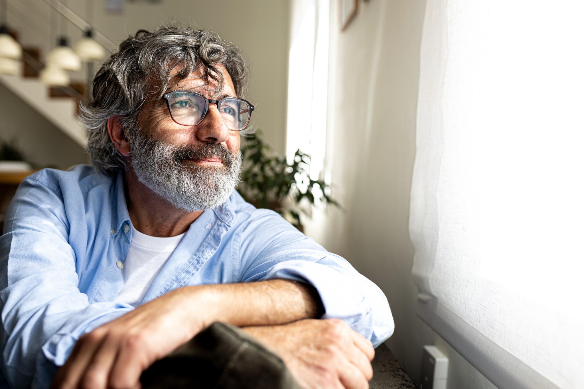 A man with gray hair and glasses sitting beside a bright window.