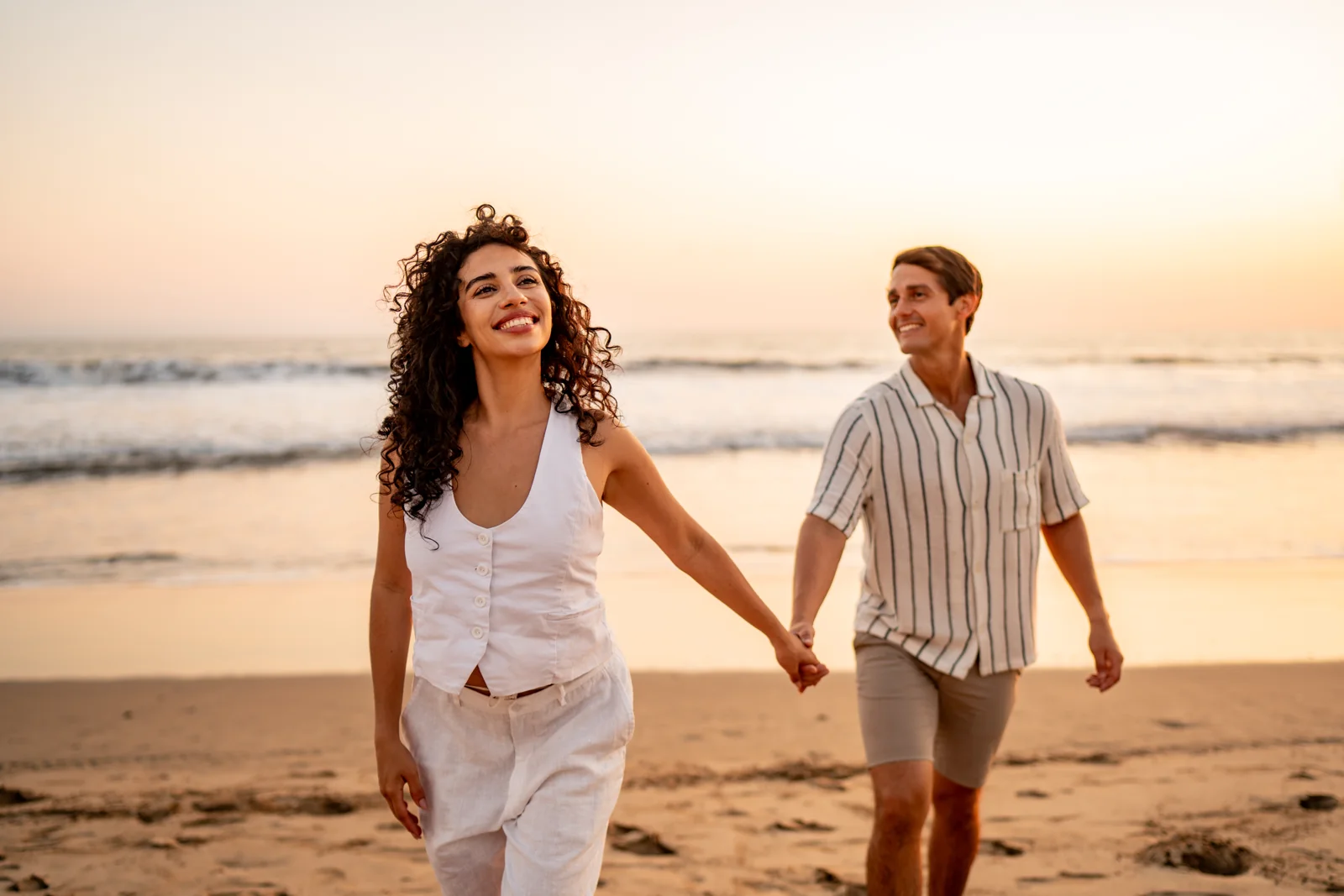 Two adults holding hands while walking along a beach at sunset.