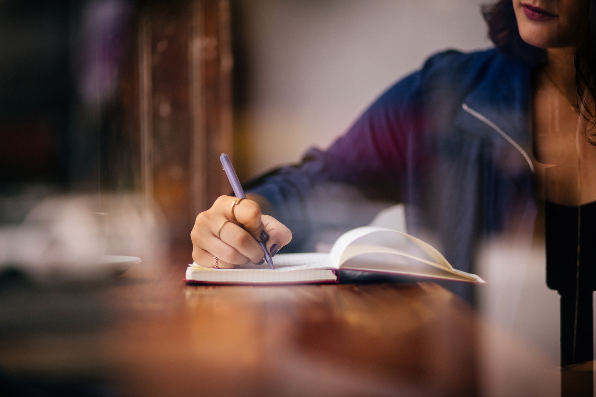 A person writing in an open notebook at a wooden counter.