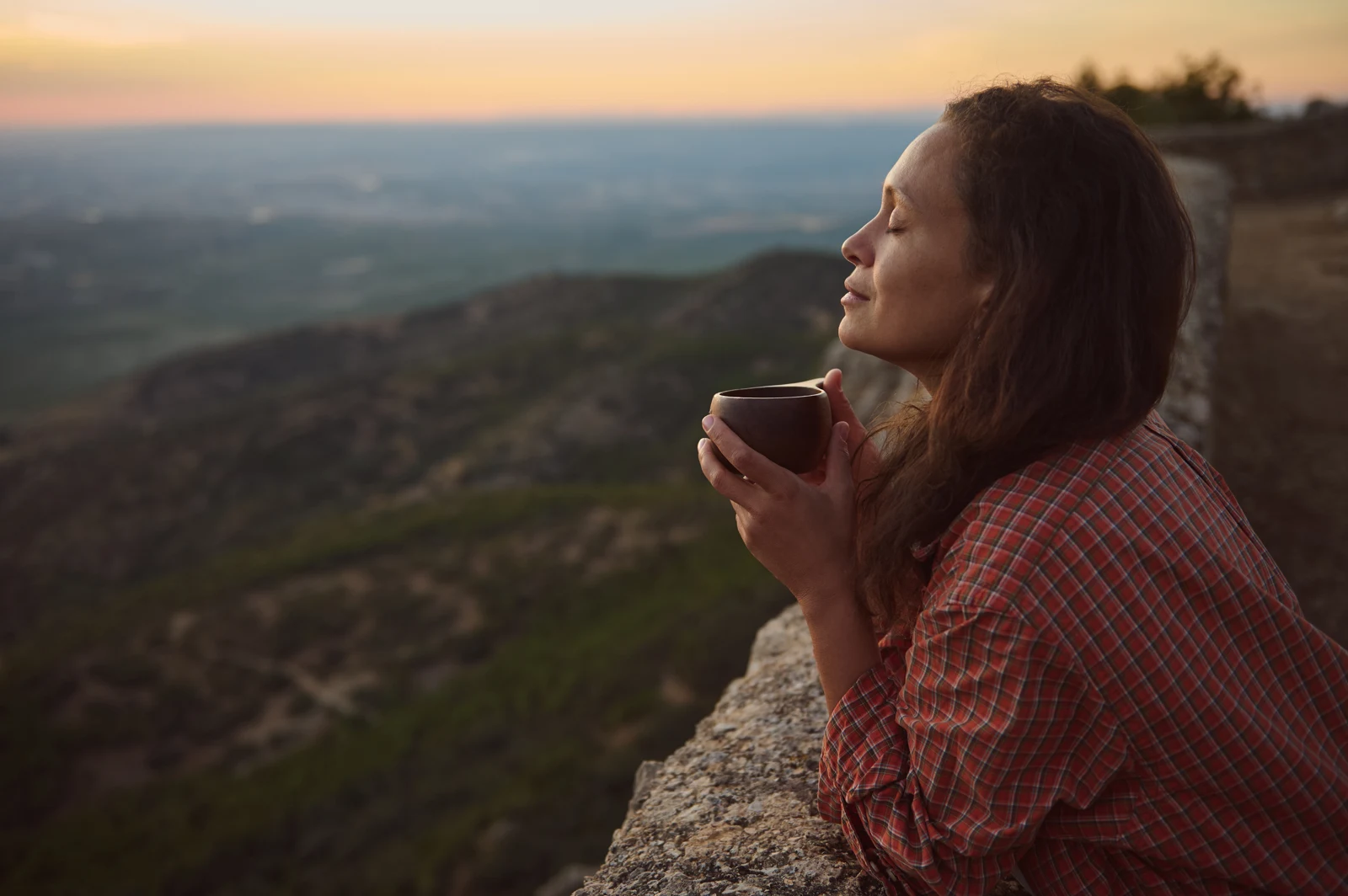 A woman holding a cup outdoors at sunset.