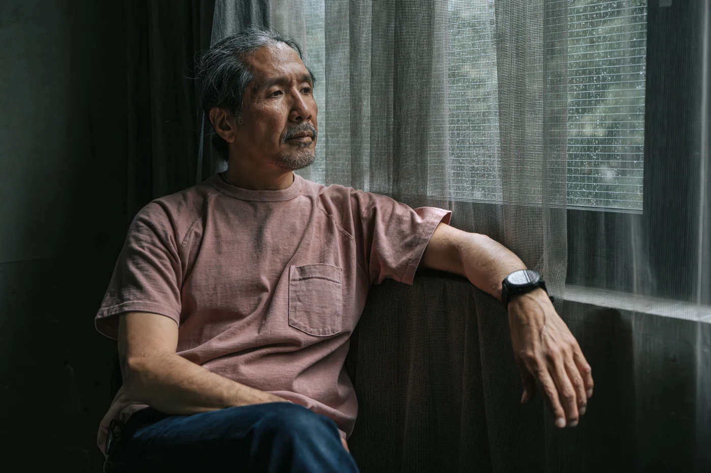 A man seated beside a window, looking outside.